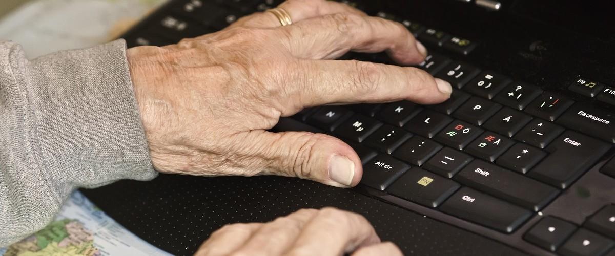 Vanhuksen kädet tietokoneen näppäimistöllä.