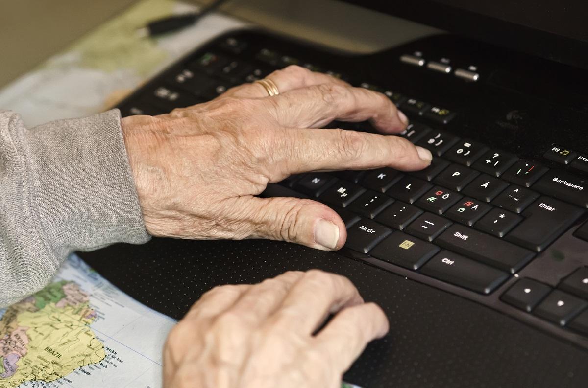 Vanhuksen kädet tietokoneen näppäimistöllä.